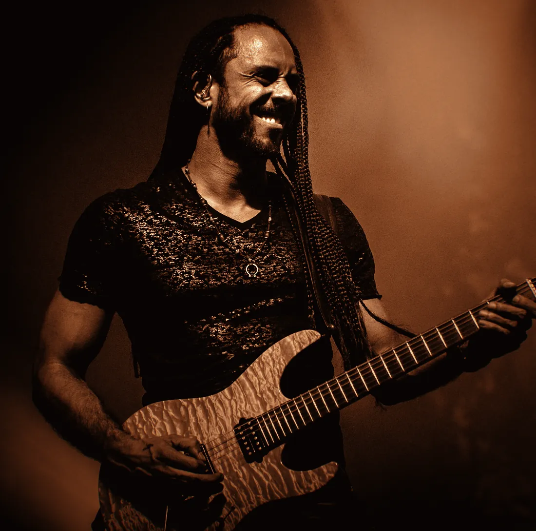Marcelo Barbosa tocando guitarra concentrado, sob luz âmbar de palco