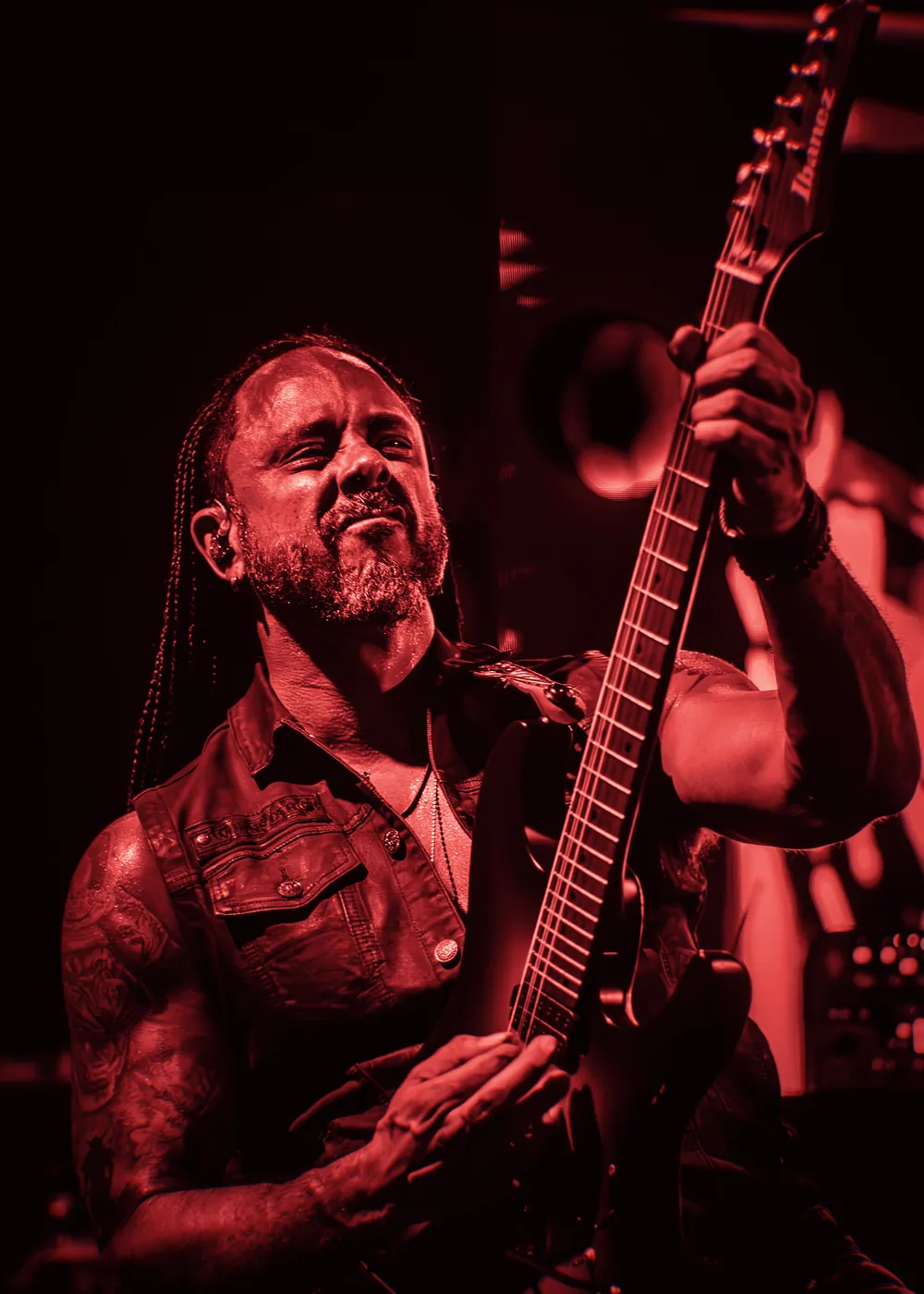 Marcelo Barbosa tocando guitarra no palco, olhando pra cima, com as tranças