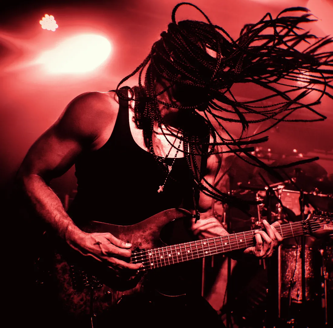 Marcelo Barbosa tocando ao vivo, com as tranças voando sob a luz vermelha do palco